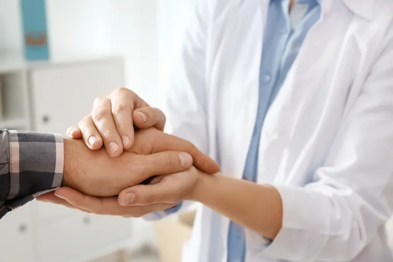 Manos con bata médica sostienen las manos de un hombre en señal de apoyo.
