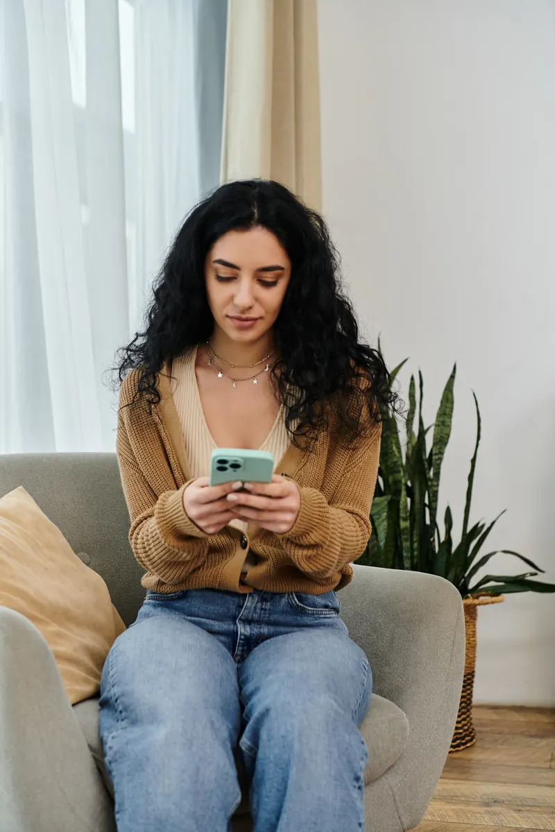 Mujer sentada en un sillón escribe un mensaje en su celular.