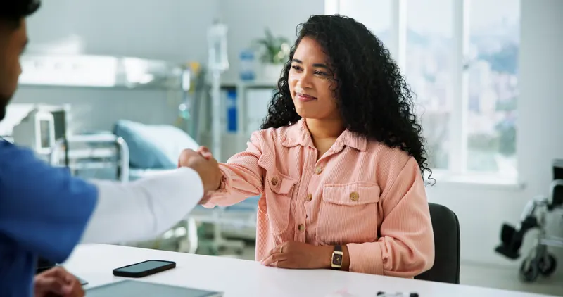 Mujer sonriente da la mano a una persona con uniforme médico en el consultorio.