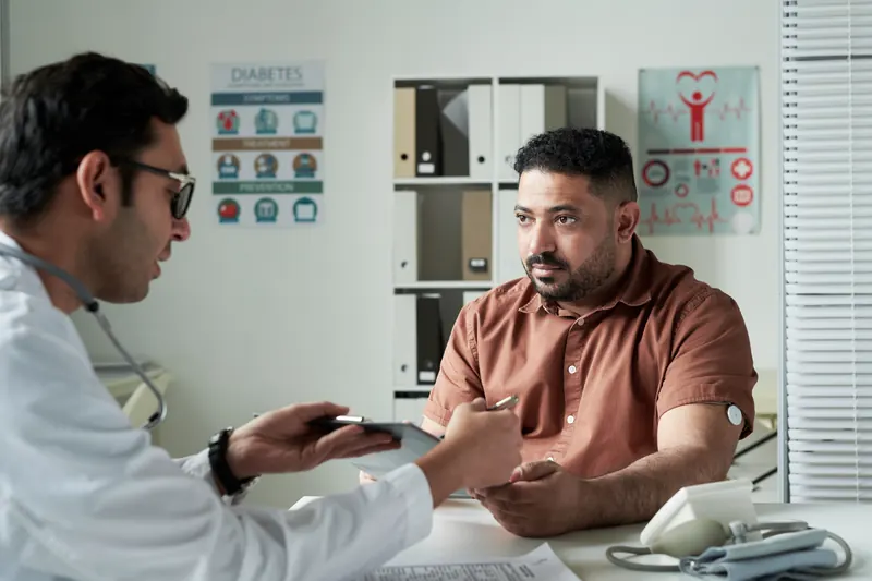 Un médico revisa unos estudios con un hombre sentado frente a su escritorio.